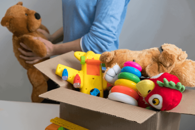 A dad holding a stuffed toy with a box of toys in front of him.
