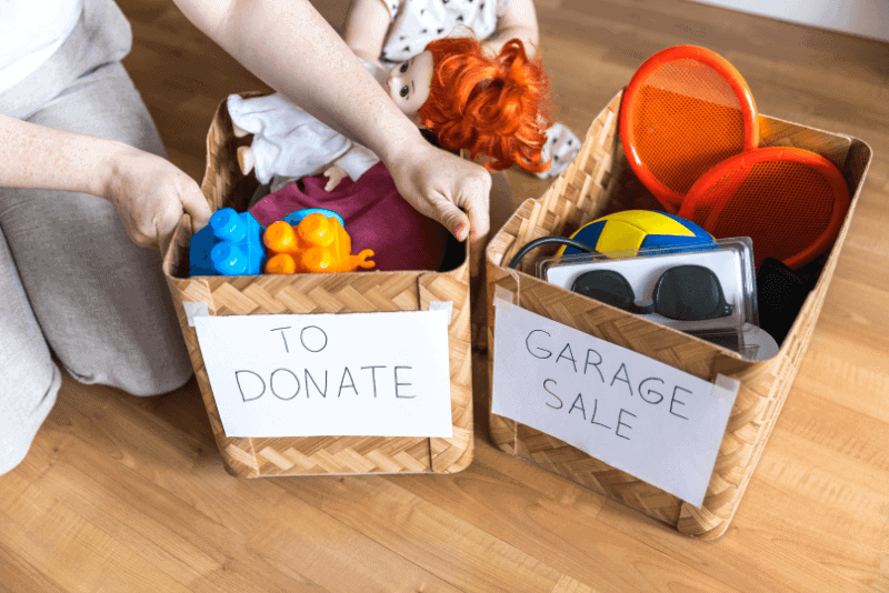 a person holding a box of "to donate" toys beside a "garage sale" toys box.